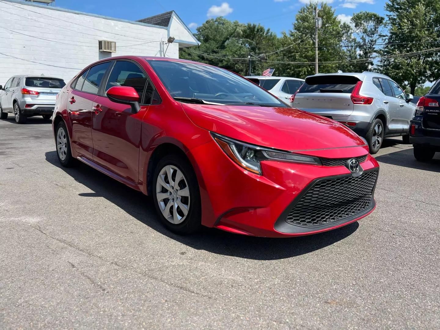 A vibrant red 2020 Toyota Corolla with a sleek exterior, featuring four doors and black interior, parked in a modern setting, showcasing its stylish design.