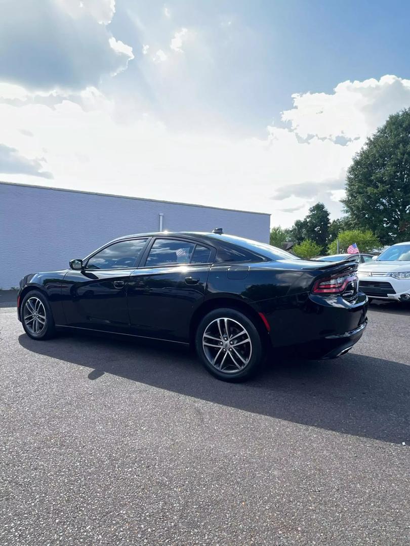 A sleek black 2019 Dodge Charger parked on a scenic road, showcasing its aggressive design and sporty silhouette under clear blue skies.