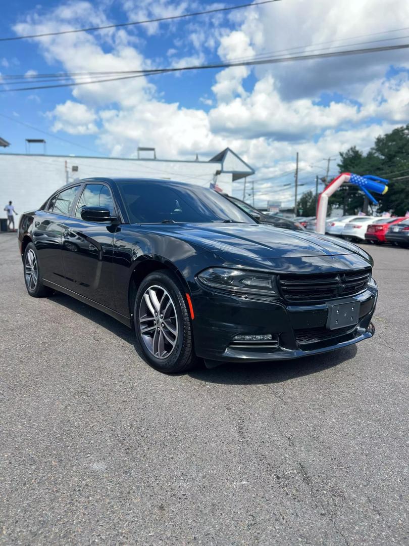 A sleek black 2019 Dodge Charger parked on a scenic road, showcasing its aggressive design and sporty silhouette under clear blue skies.