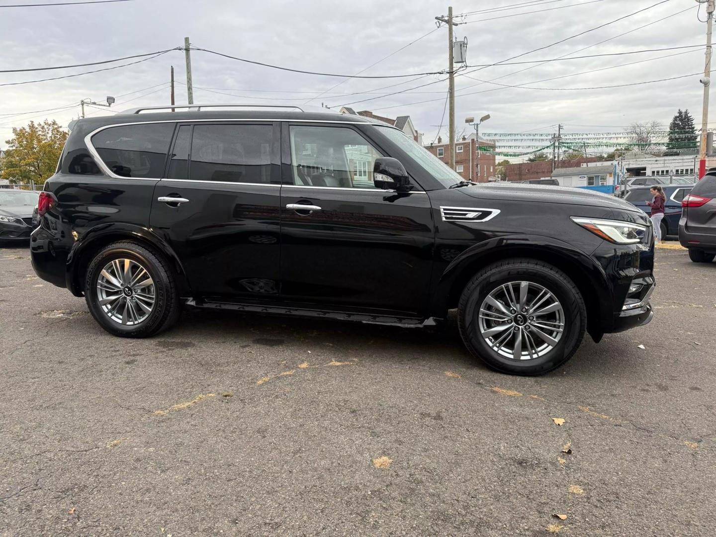 2021 INFINITI QX80 cruising a scenic mountain road, bold grille, sleek design, and LED headlights glowing at sunset.