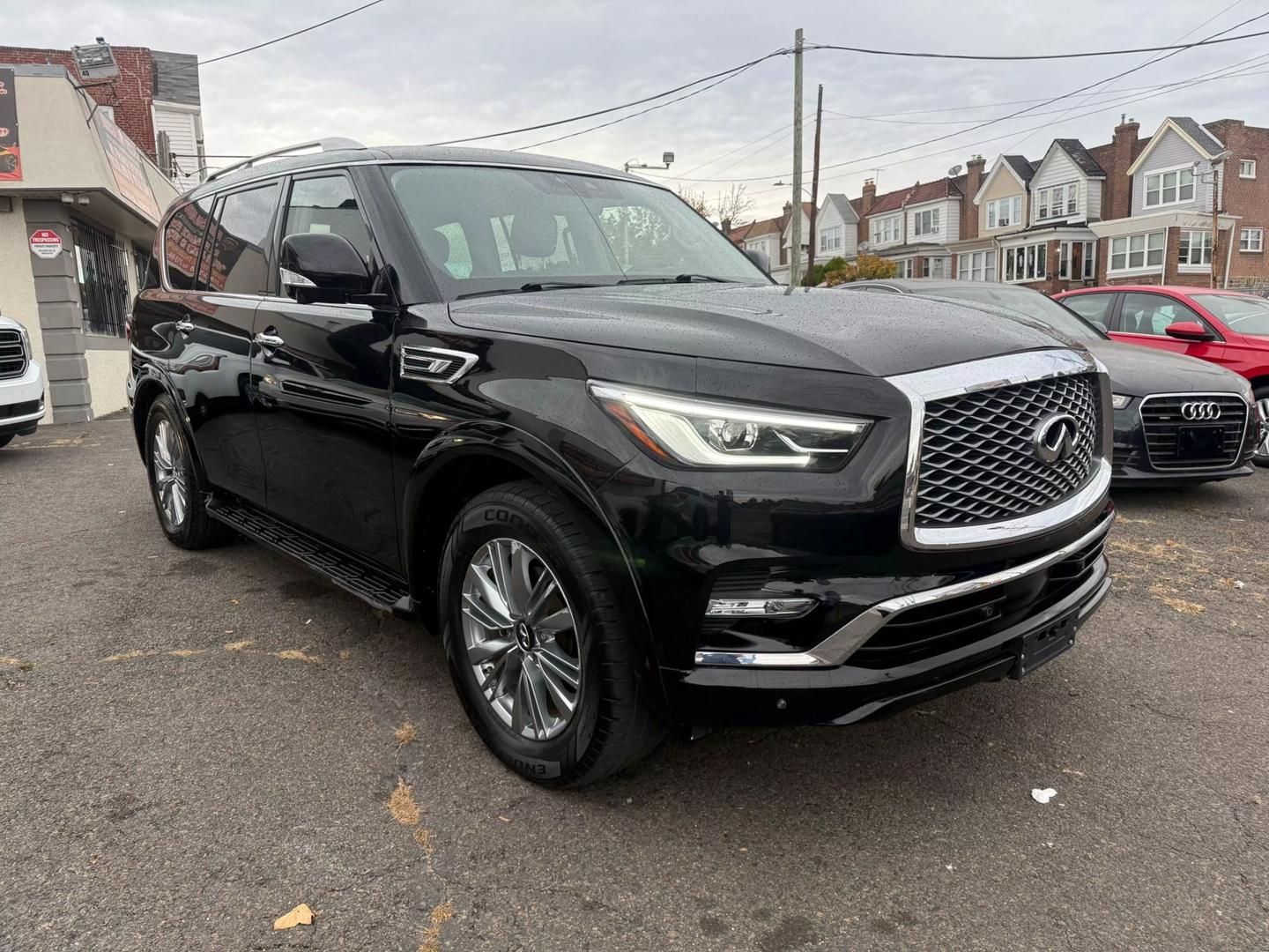 2021 INFINITI QX80 cruising a scenic mountain road, bold grille, sleek design, and LED headlights glowing at sunset.