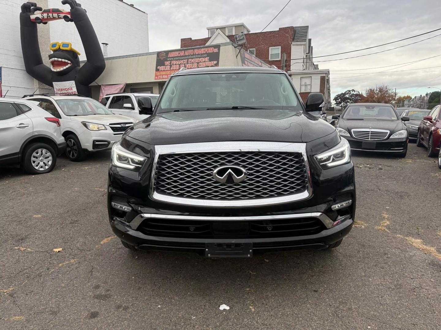 2021 INFINITI QX80 cruising a scenic mountain road, bold grille, sleek design, and LED headlights glowing at sunset.