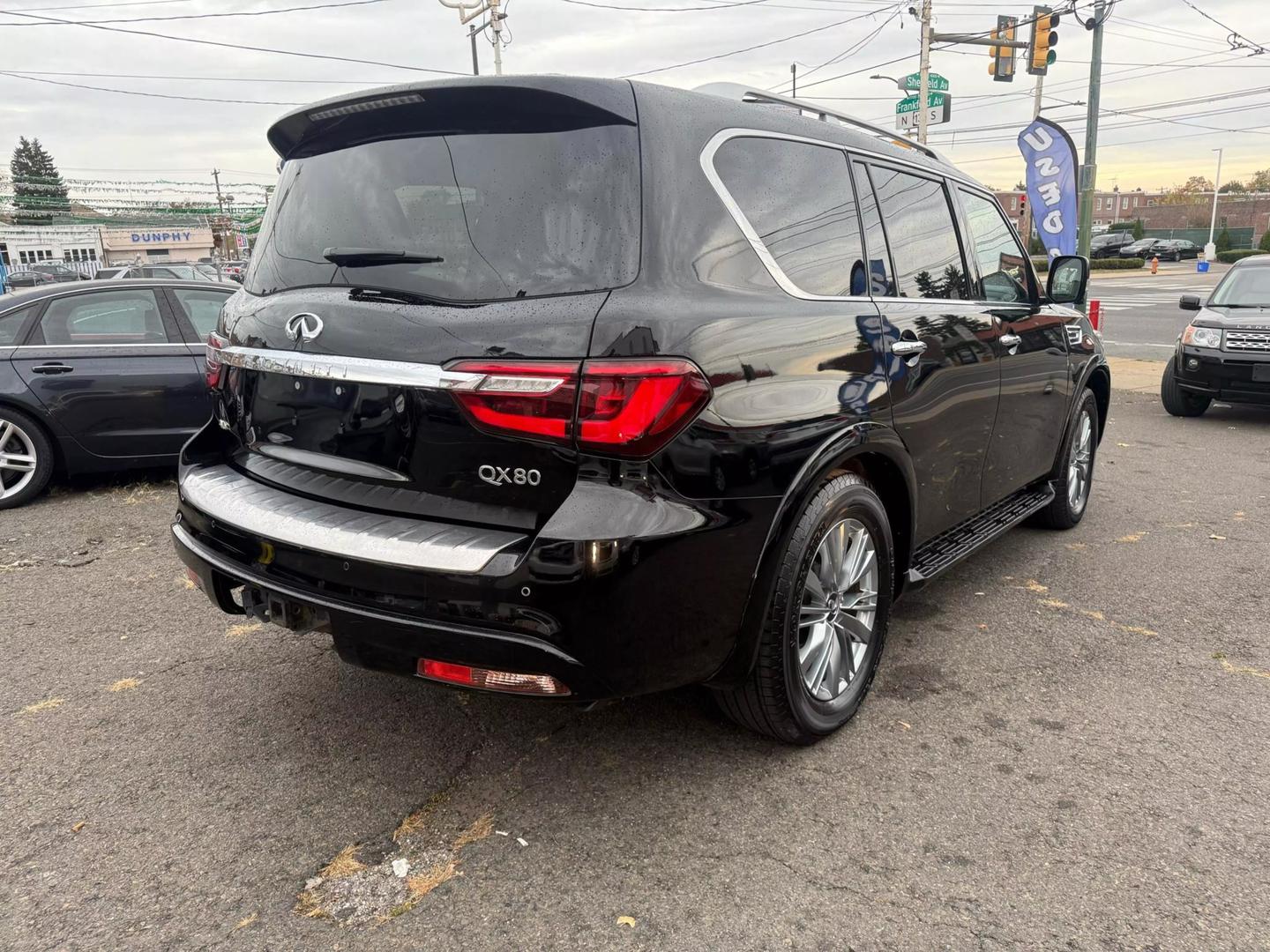 2021 INFINITI QX80 cruising a scenic mountain road, bold grille, sleek design, and LED headlights glowing at sunset.