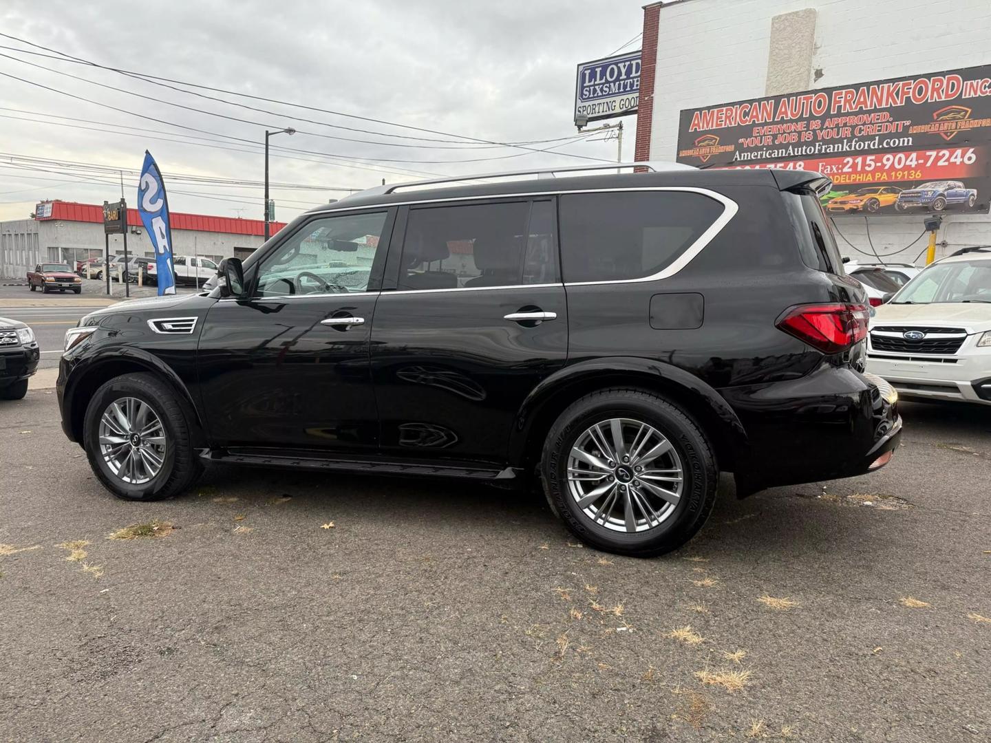 2021 INFINITI QX80 cruising a scenic mountain road, bold grille, sleek design, and LED headlights glowing at sunset.