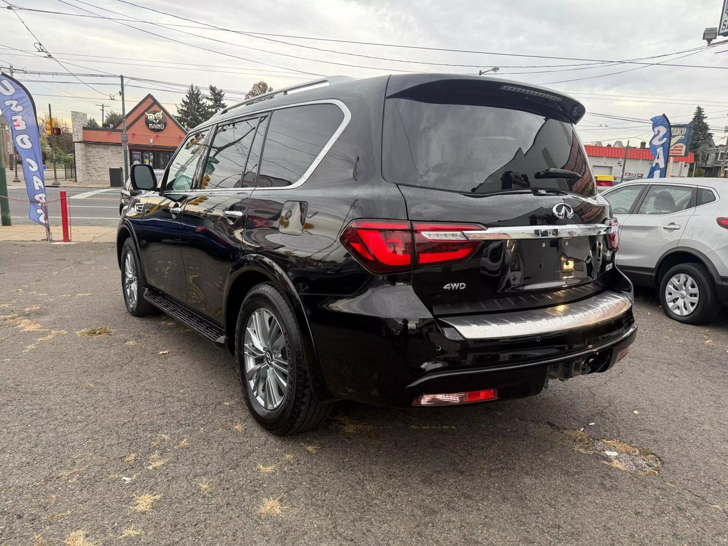 2021 INFINITI QX80 cruising a scenic mountain road, bold grille, sleek design, and LED headlights glowing at sunset.