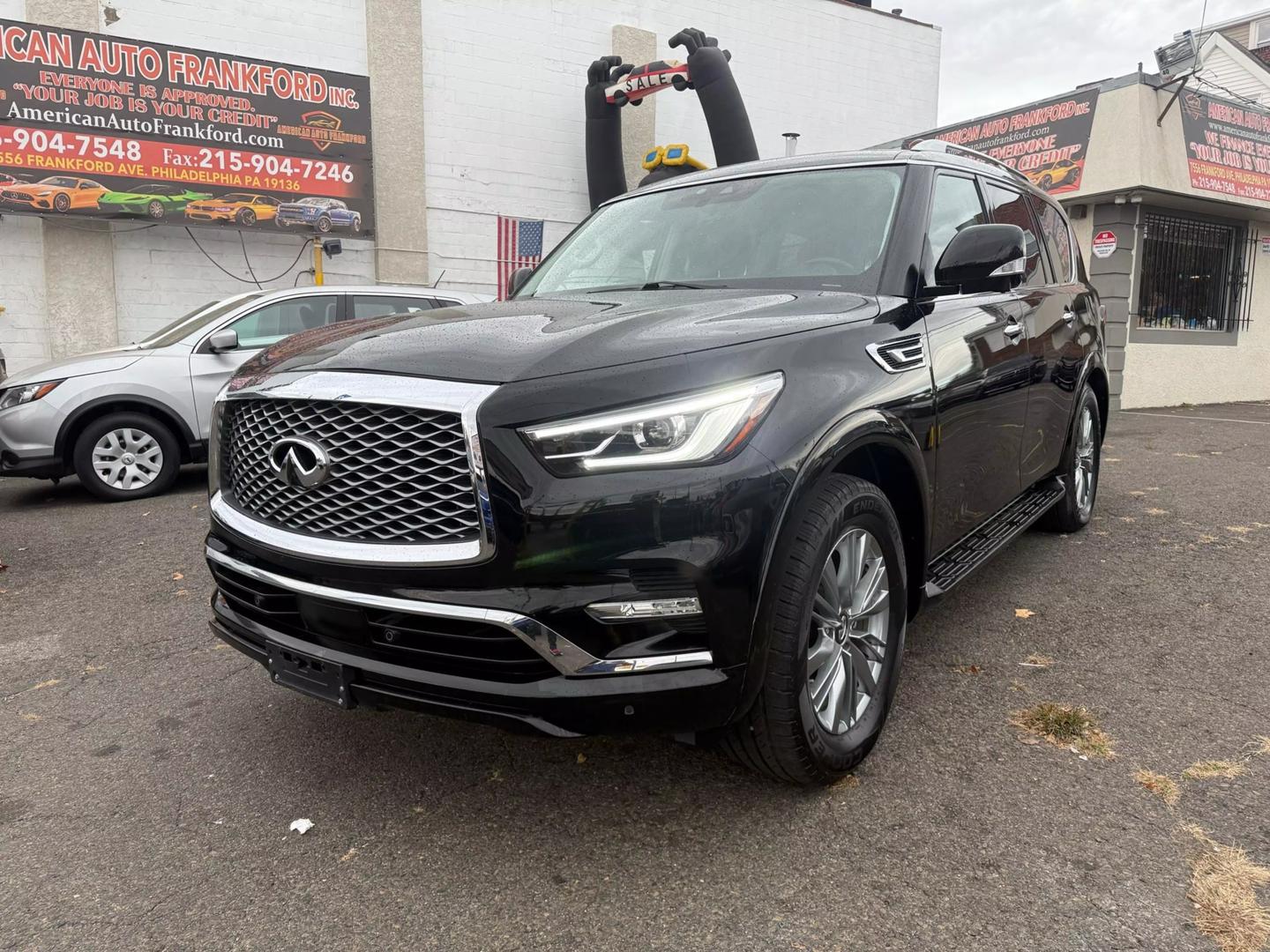 2021 INFINITI QX80 cruising a scenic mountain road, bold grille, sleek design, and LED headlights glowing at sunset.